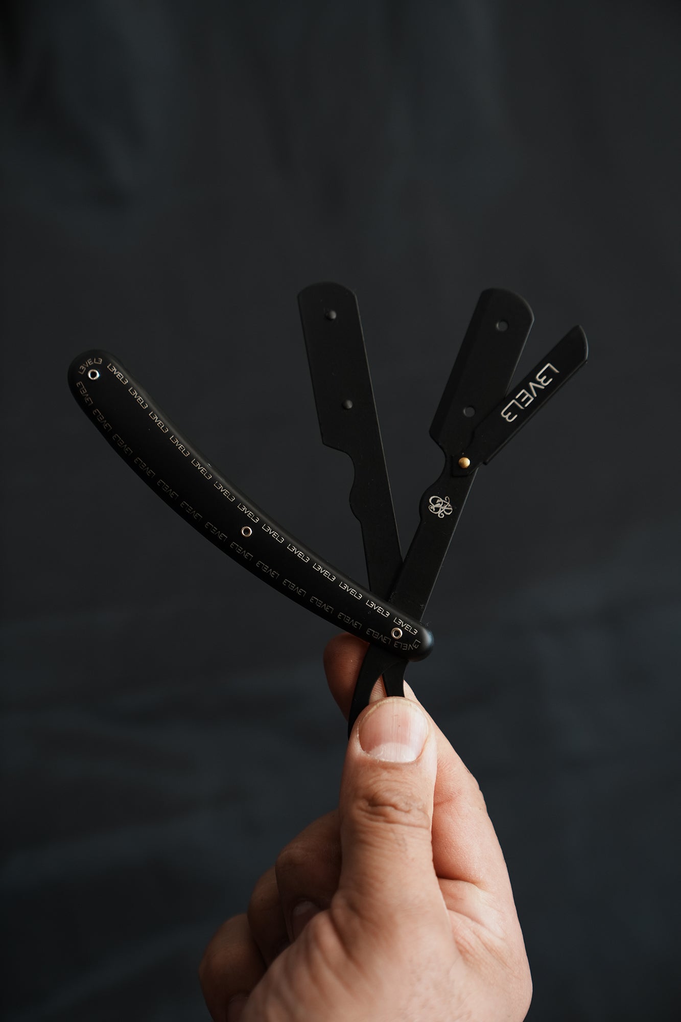 Hand holding a Level Three butterfly razor against a dark background